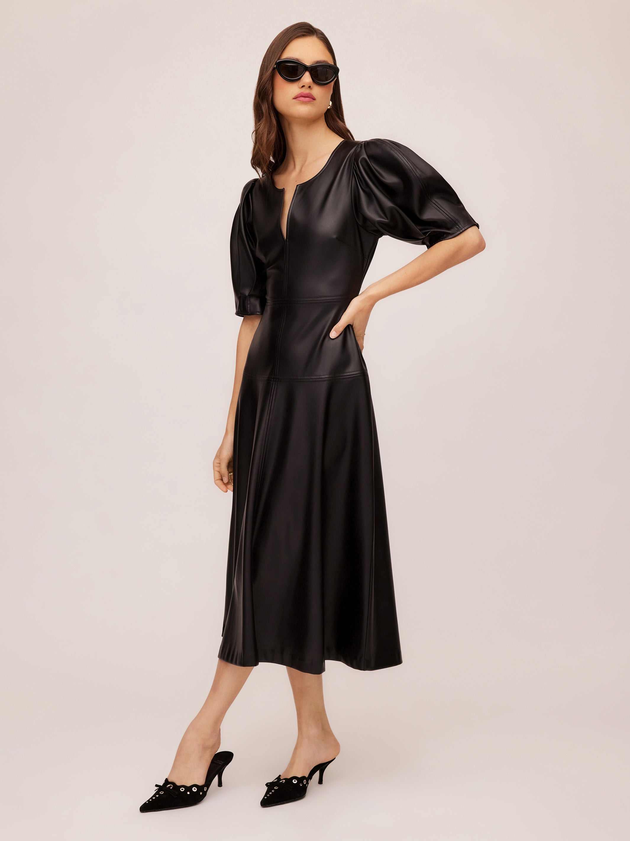 Woman wearing black Sierra Faux Leather midi dress with short peasant sleeves and split neck, styled with black heels and sunglasses