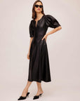 Woman wearing black Sierra Faux Leather midi dress with short peasant sleeves and split neck, styled with black heels and sunglasses
