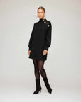 Woman wearing black Brenna Mock Neck Dress with gold button shoulder detail and long sleeves
