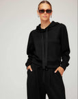 Woman wearing black Nyri Pleat Sleeve Hoodie with long pleated sleeves and drawstring hood