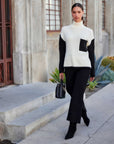 Woman wearing Colette Turtleneck Sweater with black sleeves and pocket, paired with black pants and handbag, walking outdoors