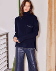 Woman wearing navy Sylvie Edge Stitch Sweater with turtleneck, drop shoulder sleeves, contrast edge stitching, and front patch pocket