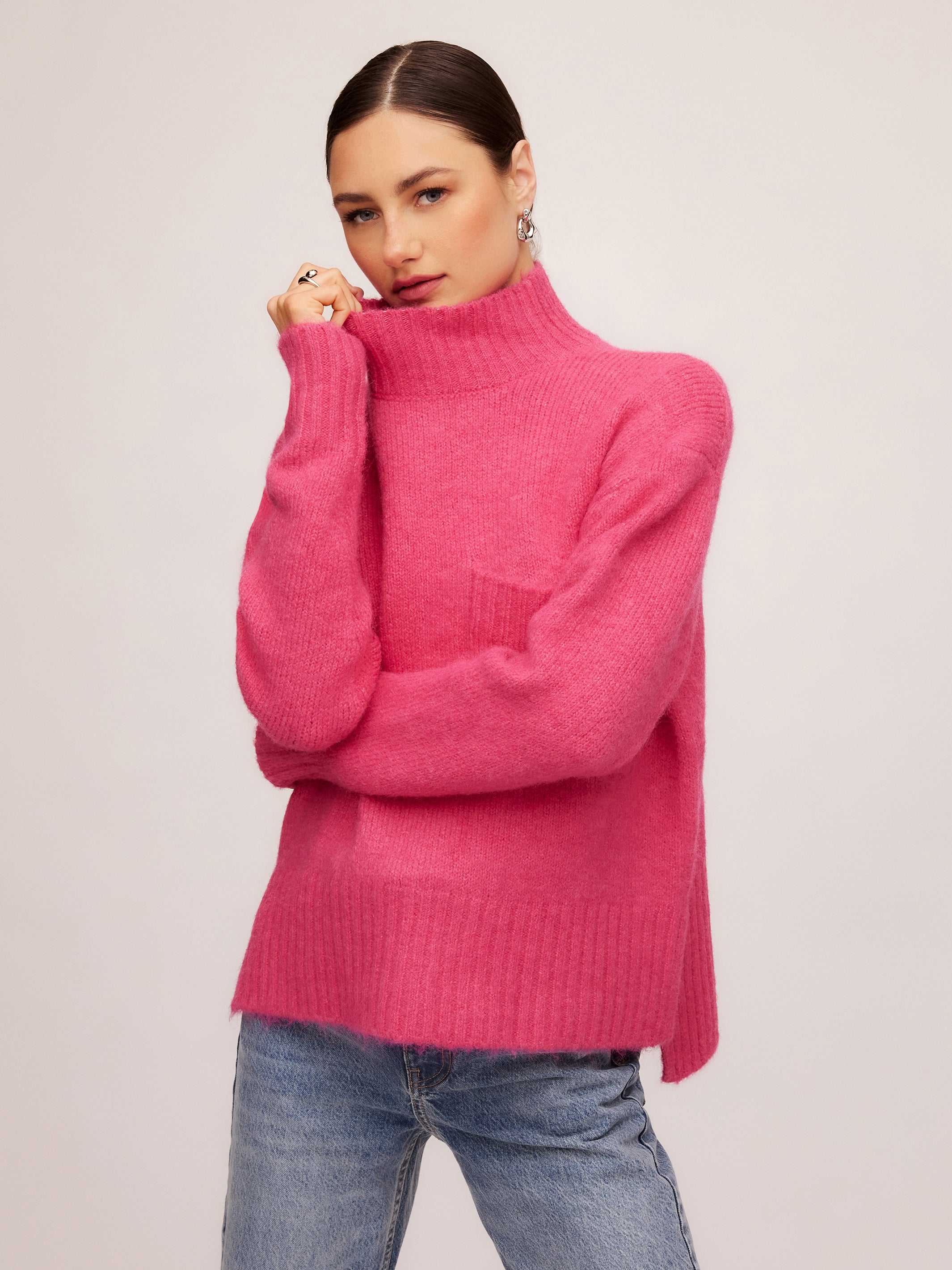Woman wearing a cozy pink Colette Turtleneck Sweater with relaxed fit, patch pocket, and hi-low hem.