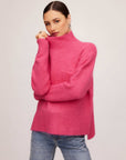 Woman wearing a cozy pink Colette Turtleneck Sweater with relaxed fit, patch pocket, and hi-low hem.