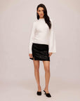 Woman wearing white Brielle flare sleeve sweater with mock neck and black skirt