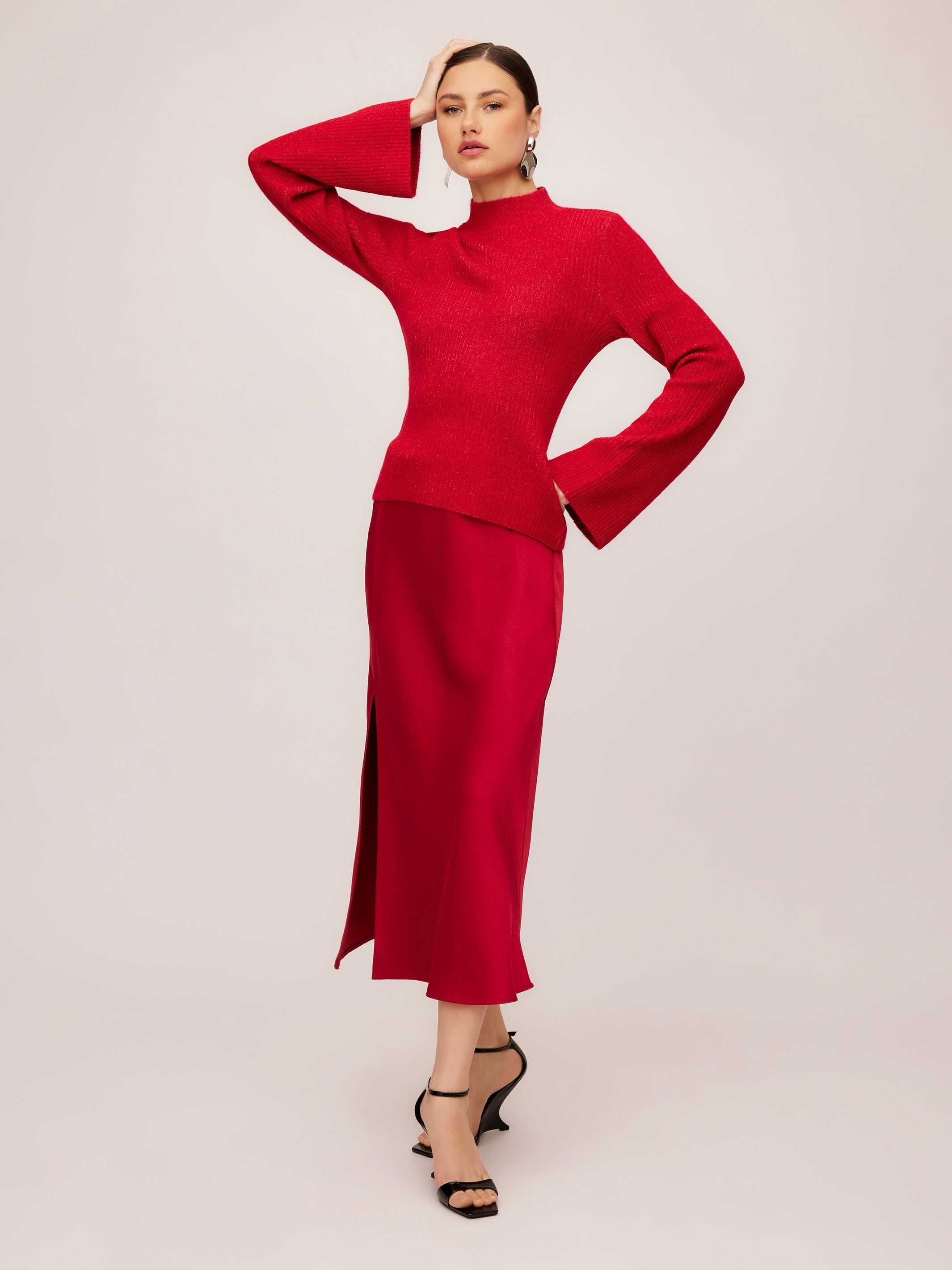 Woman wearing a red Brielle Flare Sleeve Sweater with a mock neck and ribbed knit detail paired with a matching red skirt and black heels.