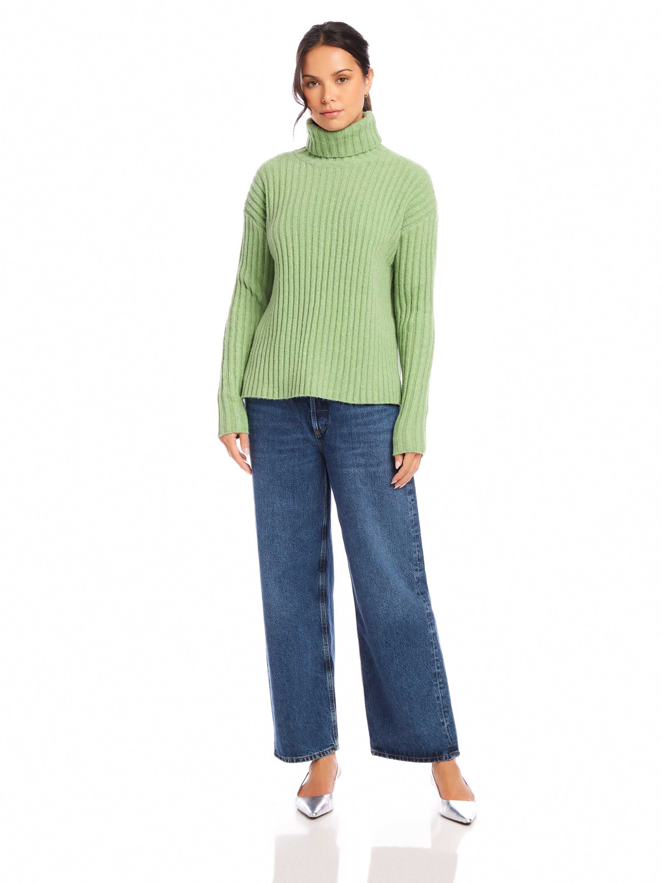 Woman wearing sage green Claudia Turtleneck Sweater with wide rib detail and blue jeans.