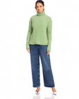 Woman wearing sage green Claudia Turtleneck Sweater with wide rib detail and blue jeans.