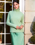 Woman wearing a sage green Claudia Turtleneck Sweater with wide rib detail and side slits outdoors