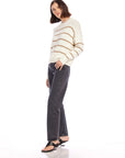 Woman wearing Luca Crewneck Sweater with beige stripes, paired with black jeans and sandals, posing against white background
