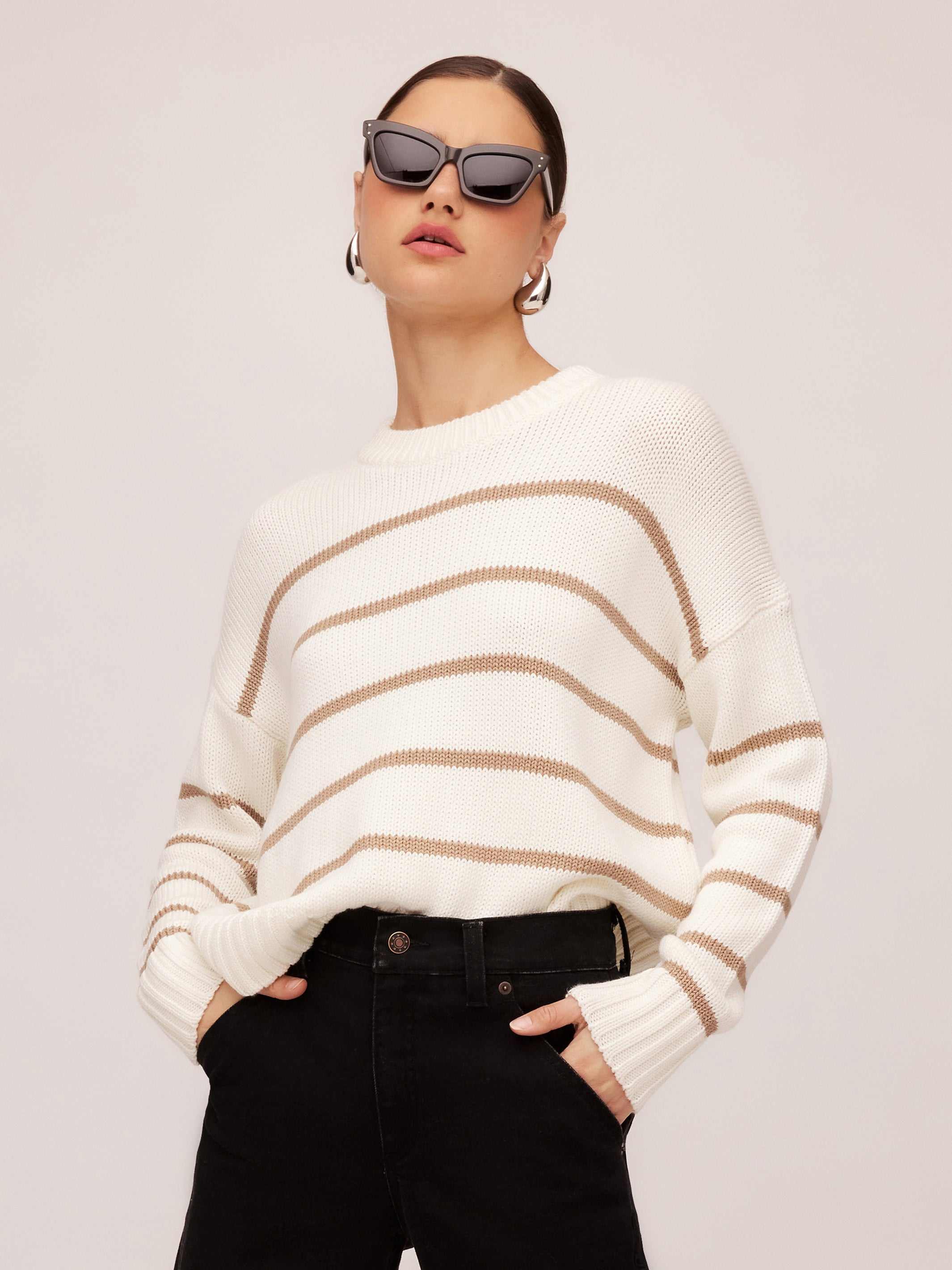 Woman wearing a white and beige striped Luca Crewneck Sweater with ribbed cuffs and hem paired with black pants and sunglasses