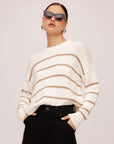 Woman wearing a white and beige striped Luca Crewneck Sweater with ribbed cuffs and hem paired with black pants and sunglasses
