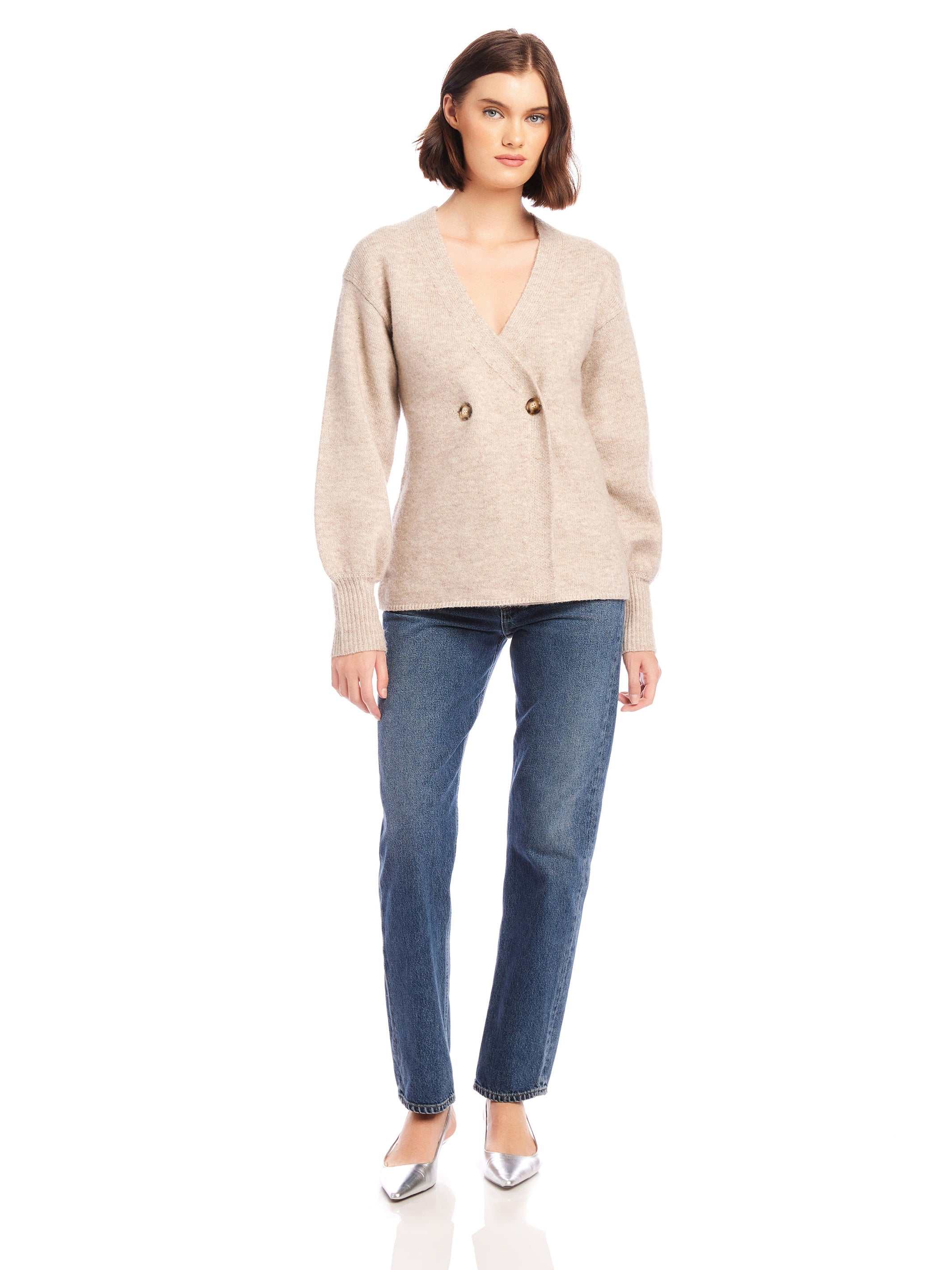 Woman wearing beige Lucy Cardigan with double-breasted buttons and wide cuffs paired with blue jeans and silver heels