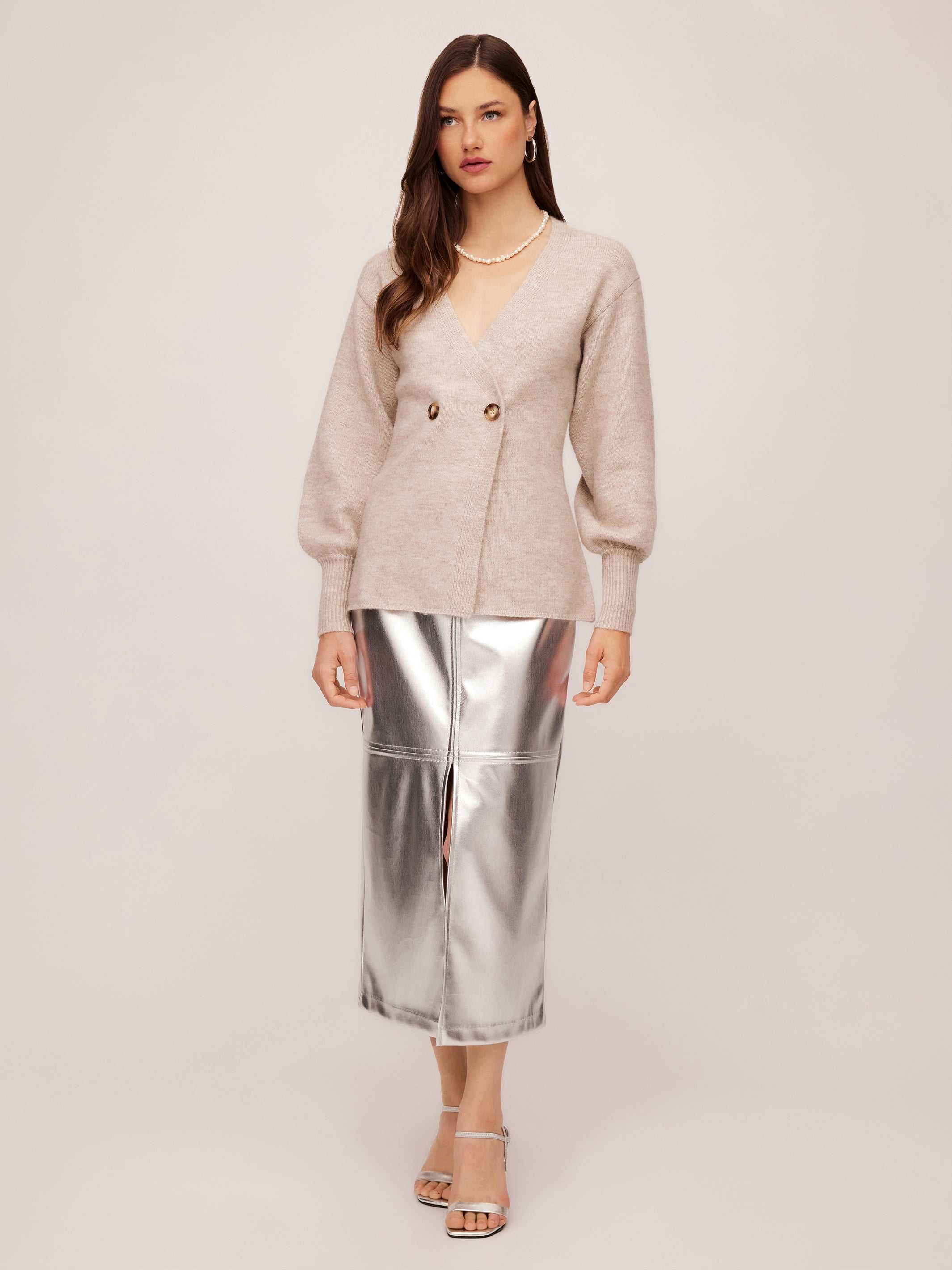Woman wearing beige Lucy Cardigan with double-breasted buttons and wide cuffs paired with silver metallic skirt