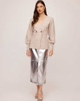 Woman wearing beige Lucy Cardigan with double-breasted buttons and wide cuffs paired with silver metallic skirt