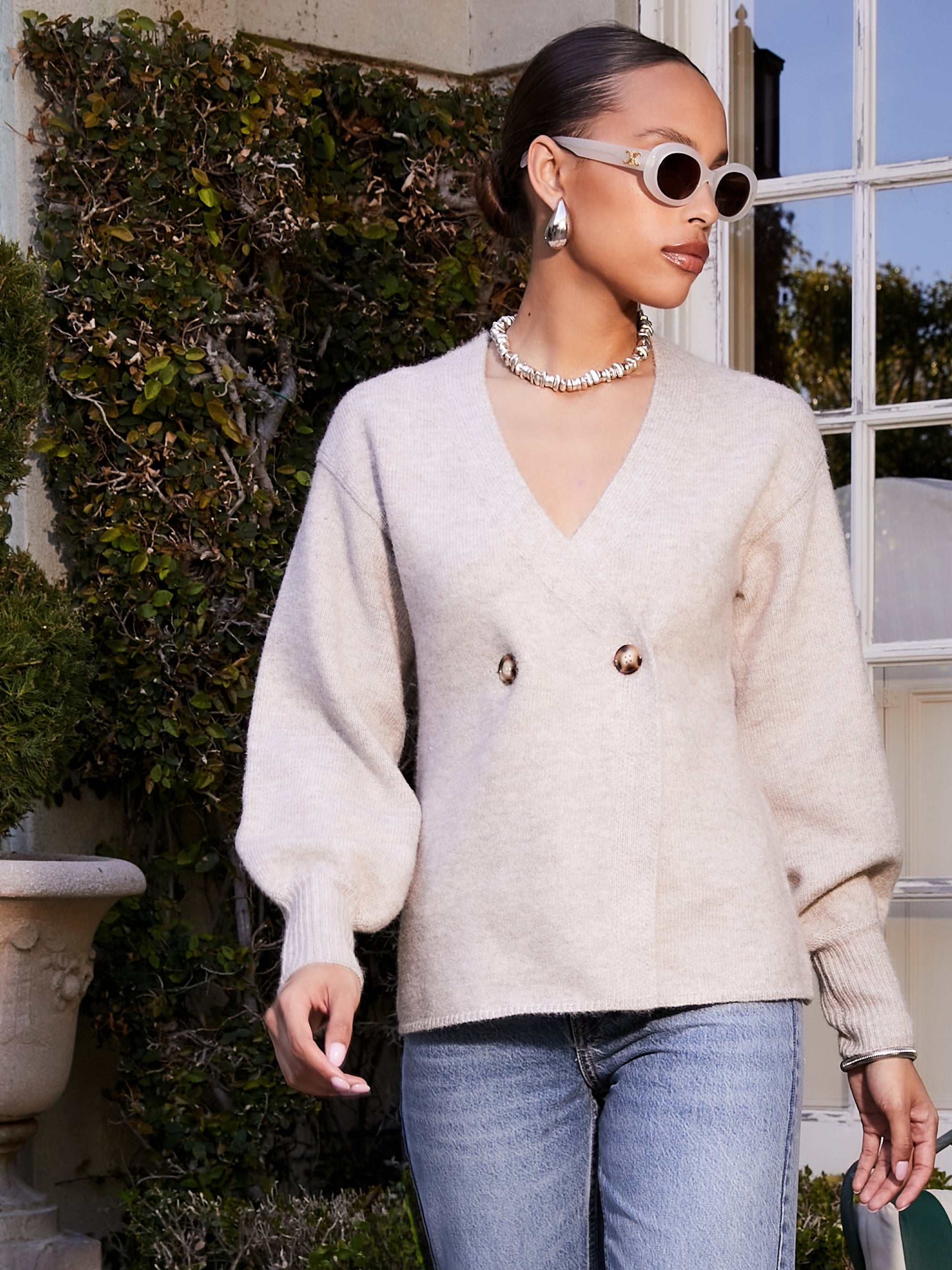 Woman wearing beige Lucy Cardigan with double-breasted buttons, V-neck, wide cuffs, and long blouson sleeves paired with jeans.