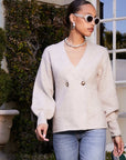 Woman wearing beige Lucy Cardigan with double-breasted buttons, V-neck, wide cuffs, and long blouson sleeves paired with jeans.