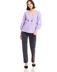 Woman wearing lavender Lucy Cardigan with double-breasted buttons, wide cuffs, V-neck, and long blouson sleeves paired with black jeans.