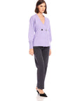 Woman wearing lavender Lucy Cardigan with V-neck, double-breasted buttons, wide cuffs, and long blouson sleeves paired with black jeans and heels