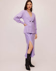 Woman wearing lavender Lucy Cardigan with double-breasted buttons, wide cuffs, and V-neck, paired with a lilac slit skirt and black boots