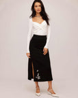 woman wearing black Brett embellished sweater skirt with beaded leaf embroidery and front slit paired with white long sleeve top