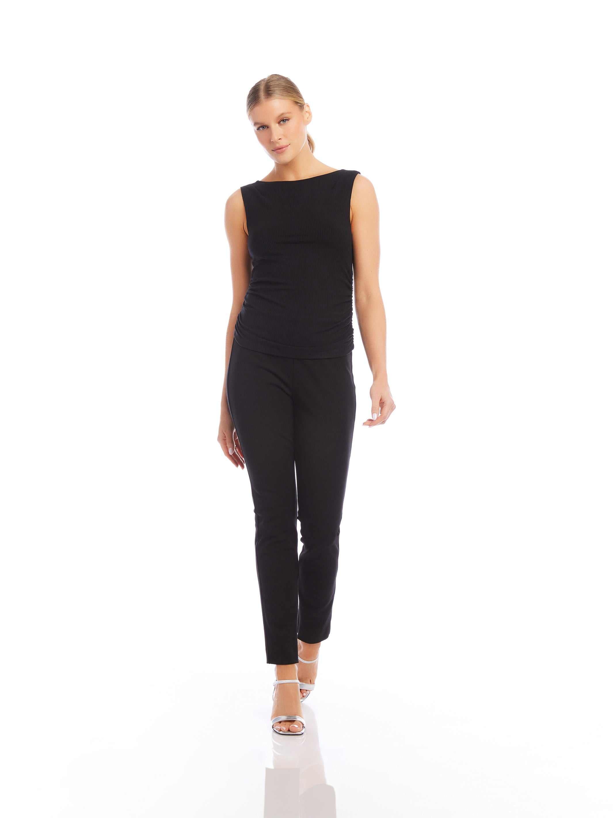 Woman wearing black Jane Ankle Zip Pants with slim fit and sleeveless black top walking on white background
