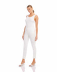Woman wearing white ankle slit pants and white tank top with white slide sandals standing on white background