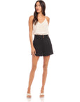 Woman wearing black Cece Pleated Trouser Shorts with front pleats and high waist, paired with white sleeveless top and sandals.