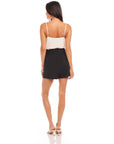 Woman wearing black Cece pleated trouser shorts with a high waist and side pockets, styled with a white camisole top and beige heels, shown from the back.