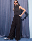 Woman wearing black Mina High Waist Pants with wide leg and front pleats, paired with sleeveless turtleneck top and sunglasses