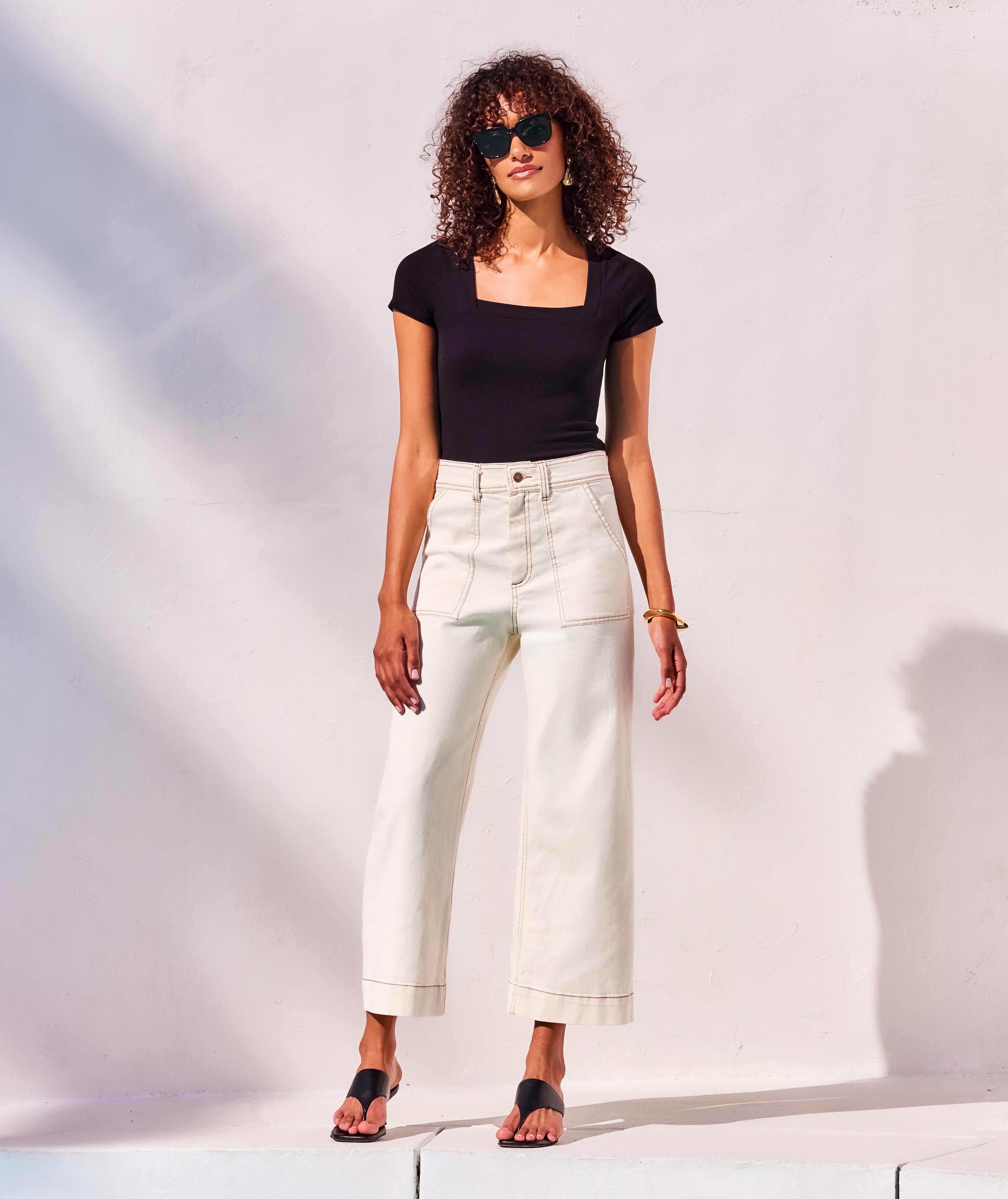 Woman wearing black Mindy T-Shirt with square neck and short sleeves paired with white pants and sunglasses outdoors