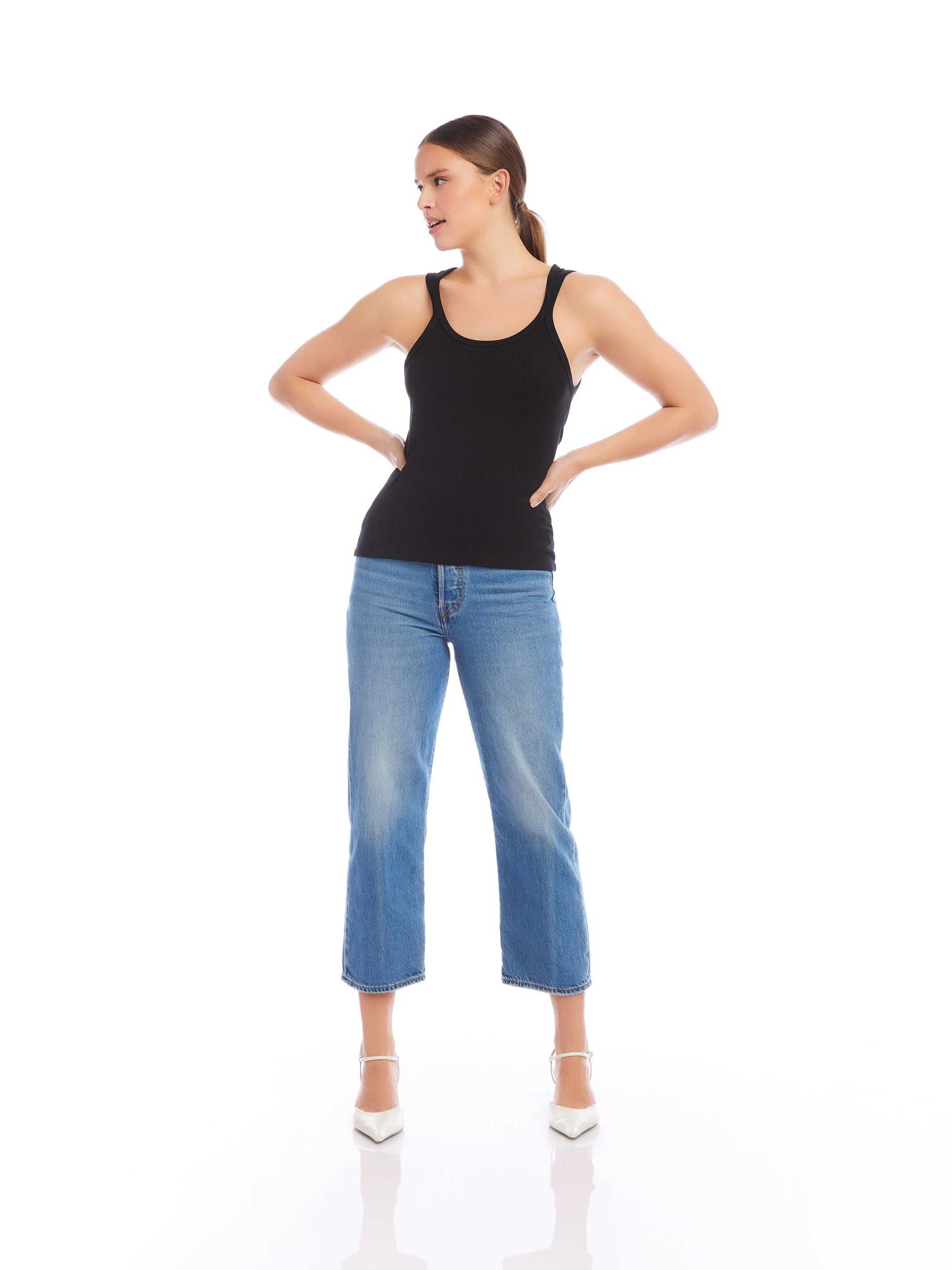 Woman wearing black bamboo rib knit Billy Tank with scoop neck and sleeveless design paired with blue cropped jeans and white heels