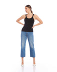 Woman wearing black bamboo rib knit Billy Tank with scoop neck and sleeveless design paired with blue cropped jeans and white heels