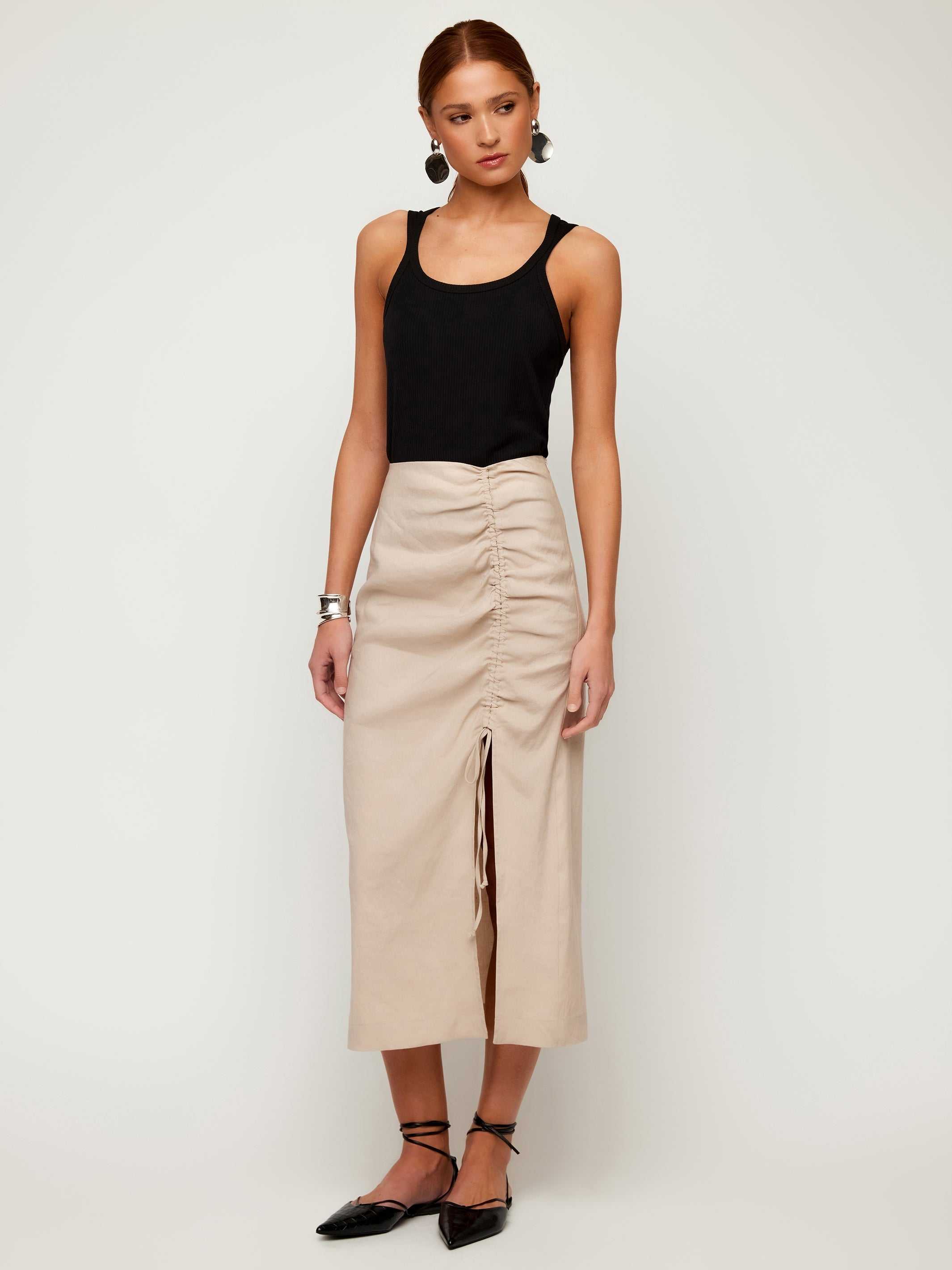 Woman wearing black Billy Tank bamboo rib knit sleeveless scoop neck top with beige ruched midi skirt and black flats