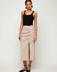 Woman wearing black Billy Tank bamboo rib knit sleeveless scoop neck top with beige ruched midi skirt and black flats