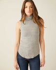 Woman wearing grey sleeveless turtleneck with rib-knit texture and shirttail hem paired with jeans