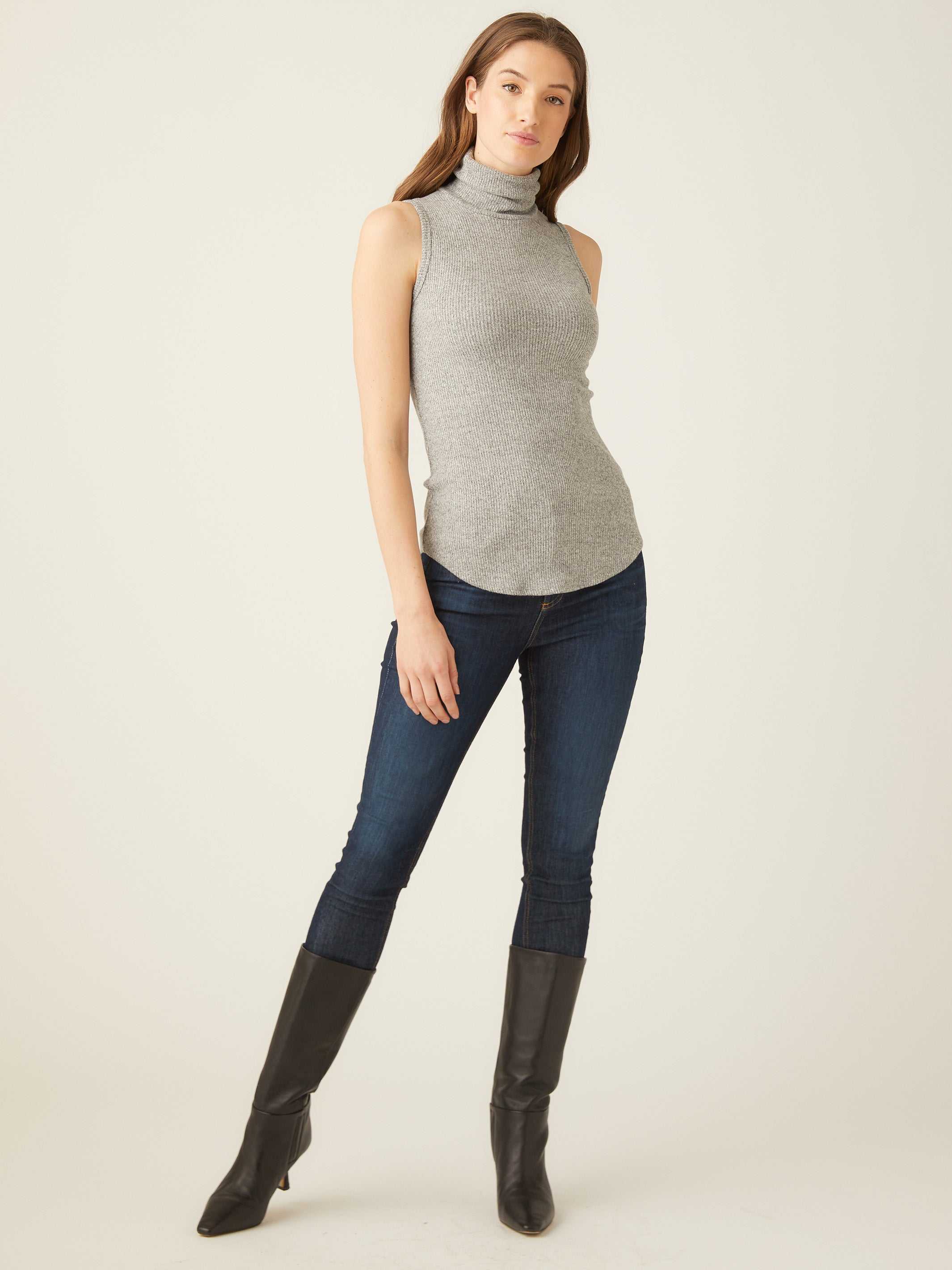 Woman wearing grey sleeveless turtleneck slim fit rib-knit top with shirttail hem and dark skinny jeans