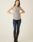Woman wearing a slim fit sleeveless turtleneck in gray with shirttail hem paired with dark jeans and black boots