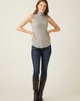 Woman wearing a slim fit sleeveless turtleneck in gray with shirttail hem paired with dark jeans and black boots