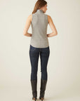 Woman wearing grey sleeveless turtleneck top with shirttail hem paired with dark jeans and black boots, back view