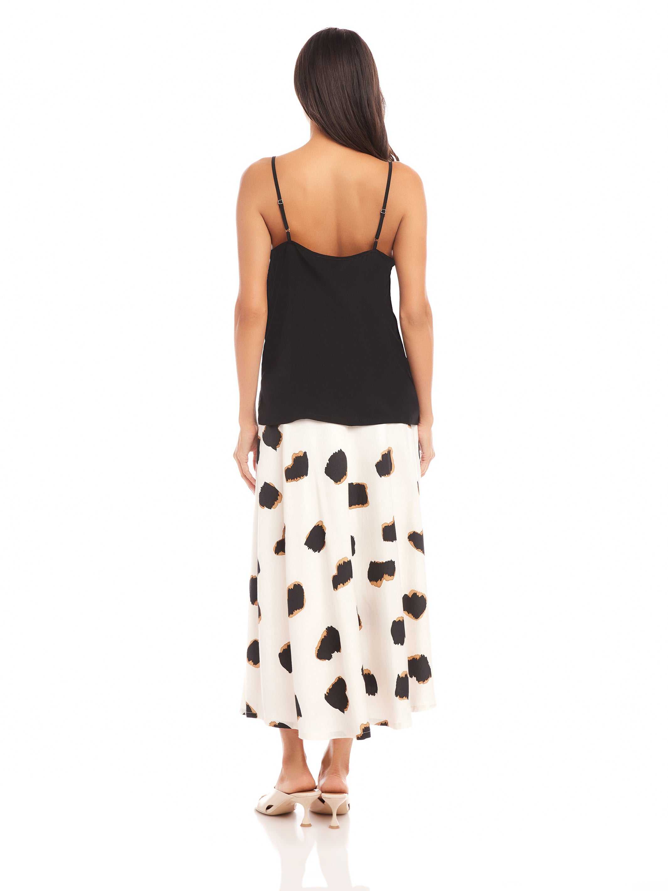 Back view of a woman wearing a black Carys Silk Cami with adjustable spaghetti straps and a flowy white skirt with black spots