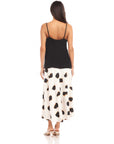 Back view of a woman wearing a black Carys Silk Cami with adjustable spaghetti straps and a flowy white skirt with black spots
