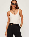 Woman wearing white Carys Silk Cami with adjustable spaghetti straps and V-neckline paired with black pants and sunglasses