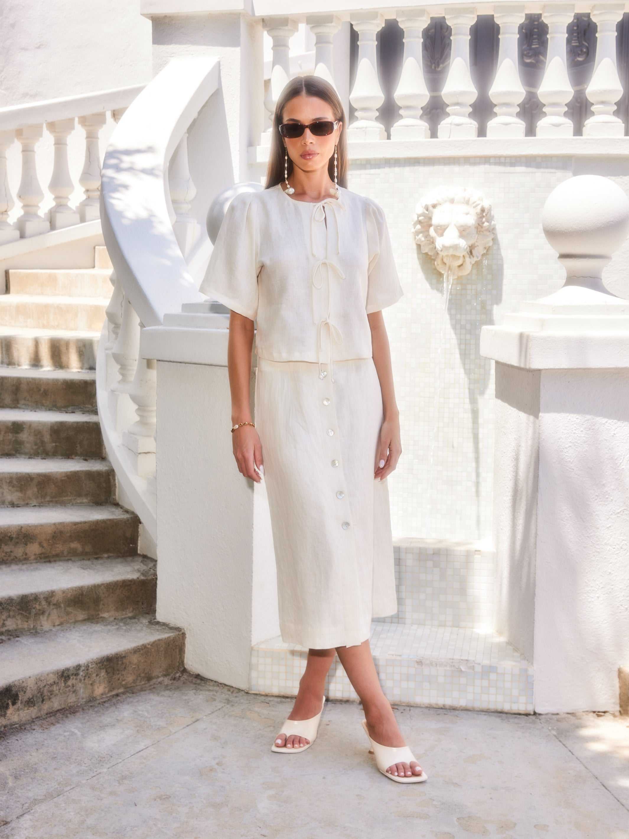 Woman wearing a white Lori Midi Skirt with front buttons and slit, styled with matching top and sunglasses in an outdoor setting
