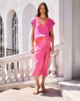 Woman wearing pink Fiona Shirred Midi Skirt with side shirring and slit standing outdoors by white balustrade