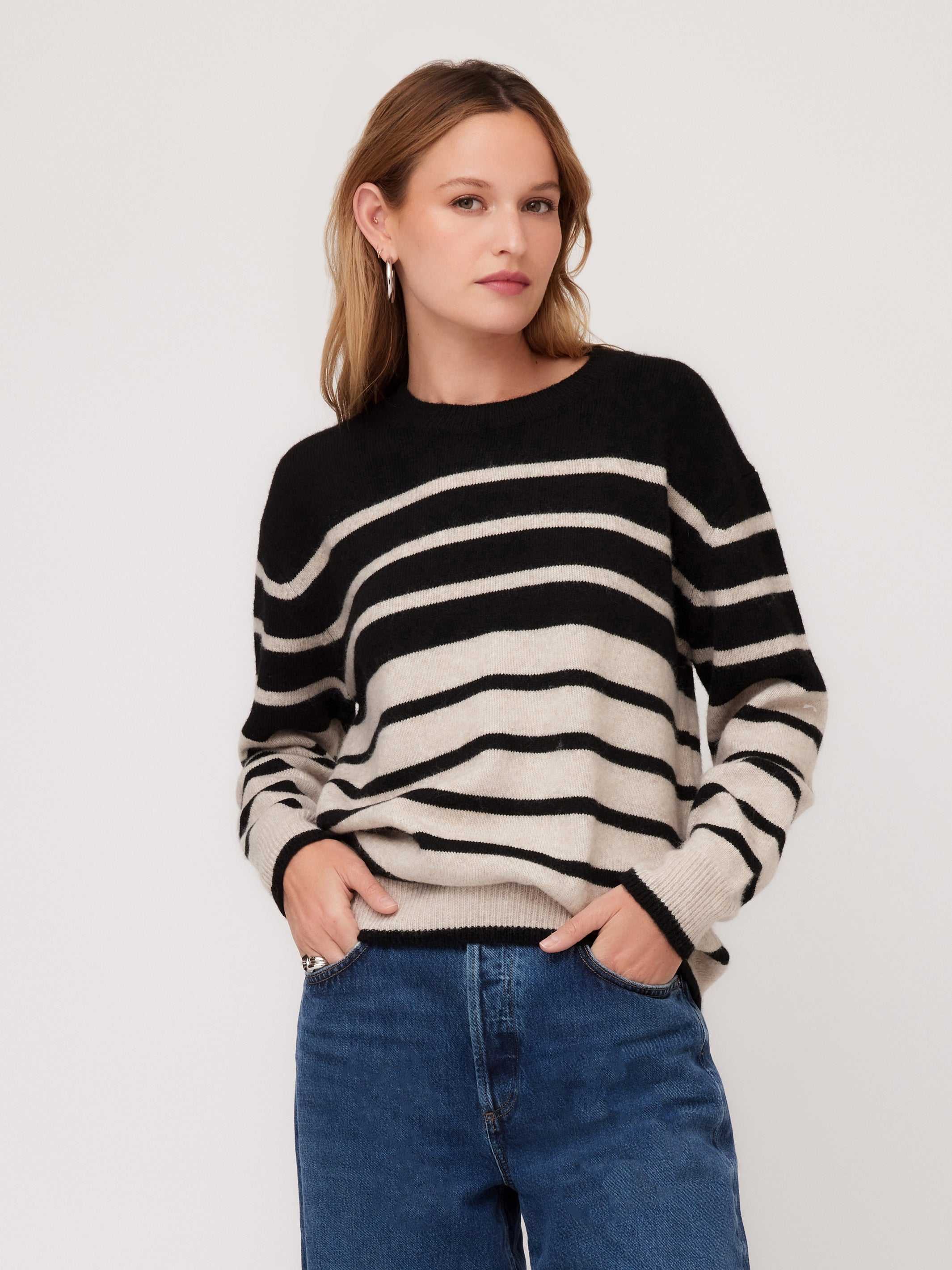 Woman wearing a black and beige striped sweater with long sleeves and blue jeans