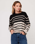 Woman wearing a black and beige striped sweater with long sleeves and blue jeans