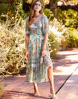 Woman wearing a colorful paisley tiered poof sleeve dress with ruffle skirt and removable waist tie outdoors