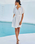 Woman wearing white short sleeve peasant dress with removable waist tie standing by pool