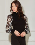 Woman wearing black sheer sleeve top with turtleneck and patterned long blouson sleeves